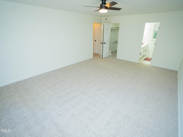 unfurnished bedroom featuring ensuite bath, light carpet, ceiling fan, a closet, and a spacious closet