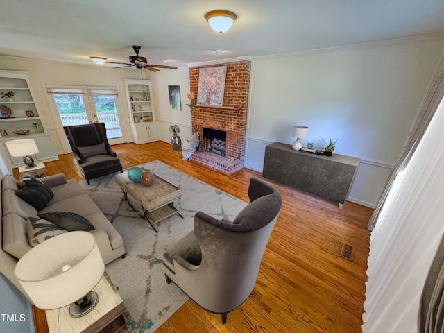 living room featuring hardwood / wood-style flooring, built in shelves, ceiling fan, a fireplace, and crown molding