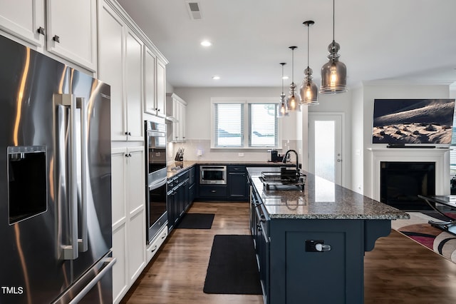 kitchen with pendant lighting, white cabinetry, a center island with sink, appliances with stainless steel finishes, and dark hardwood / wood-style flooring