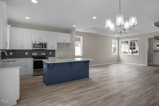 kitchen featuring appliances with stainless steel finishes, a sink, a kitchen island, white cabinetry, and light wood-style floors