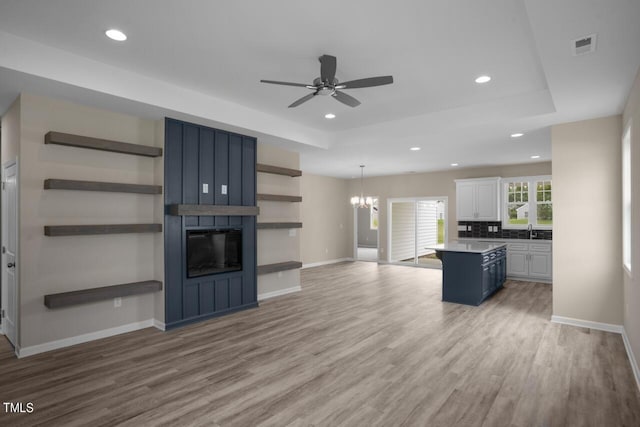 unfurnished living room with wood finished floors, recessed lighting, baseboards, ceiling fan, and a raised ceiling