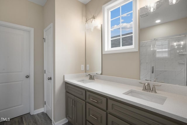 bathroom featuring a shower stall, double vanity, wood finished floors, and baseboards