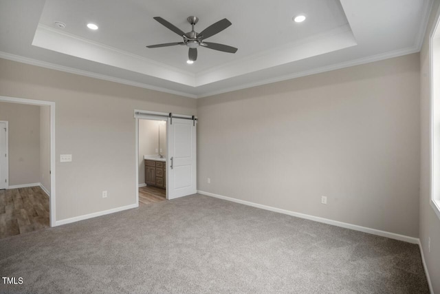 unfurnished bedroom featuring a raised ceiling, carpet, ornamental molding, a barn door, and baseboards