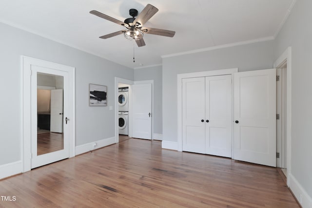 unfurnished bedroom with crown molding, hardwood / wood-style flooring, stacked washer and dryer, and ceiling fan