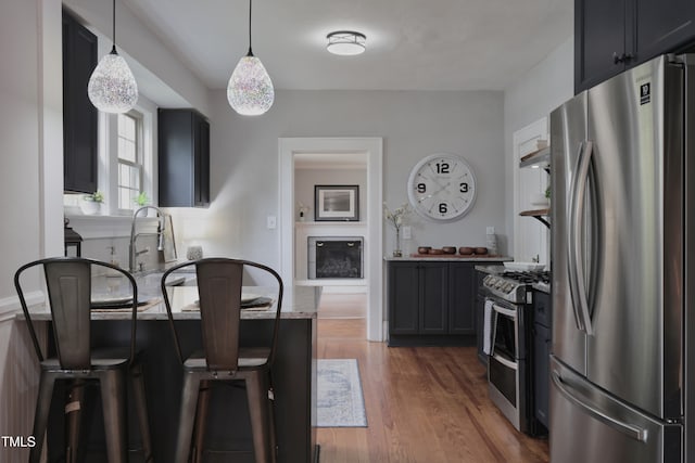 kitchen with light stone countertops, appliances with stainless steel finishes, dark hardwood / wood-style flooring, decorative light fixtures, and a breakfast bar area