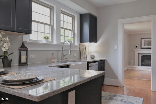 kitchen with light stone countertops, stainless steel dishwasher, light hardwood / wood-style flooring, ornamental molding, and sink