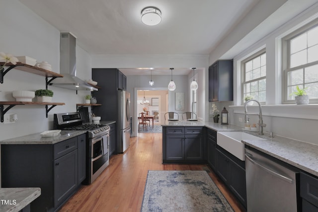 kitchen with exhaust hood, kitchen peninsula, stainless steel appliances, sink, and light hardwood / wood-style floors