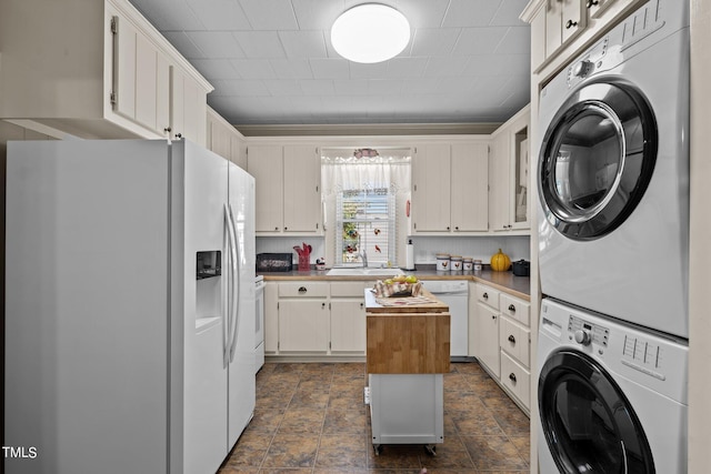 kitchen with a center island, white appliances, sink, white cabinetry, and stacked washer and dryer