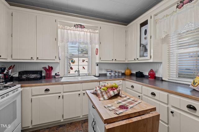 kitchen featuring white cabinets, stacked washer / dryer, sink, and white range oven