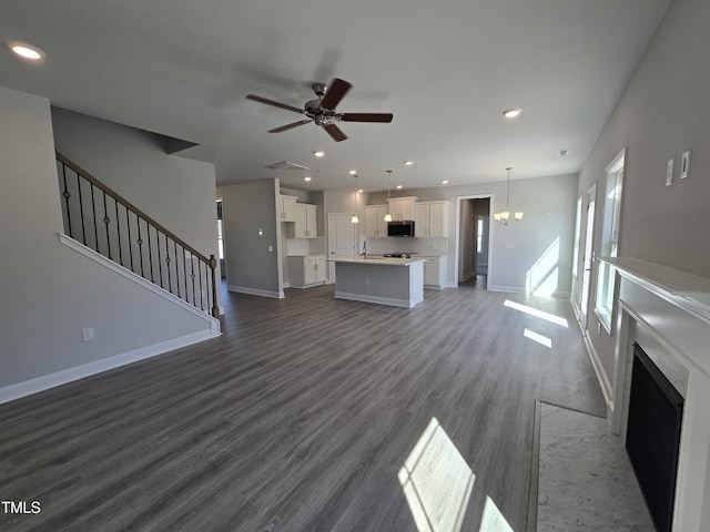 unfurnished living room with ceiling fan, a sink, baseboards, stairway, and dark wood-style floors