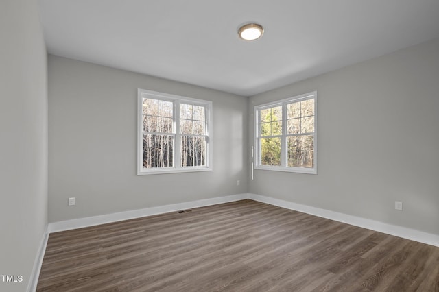 unfurnished room with visible vents, dark wood finished floors, and baseboards