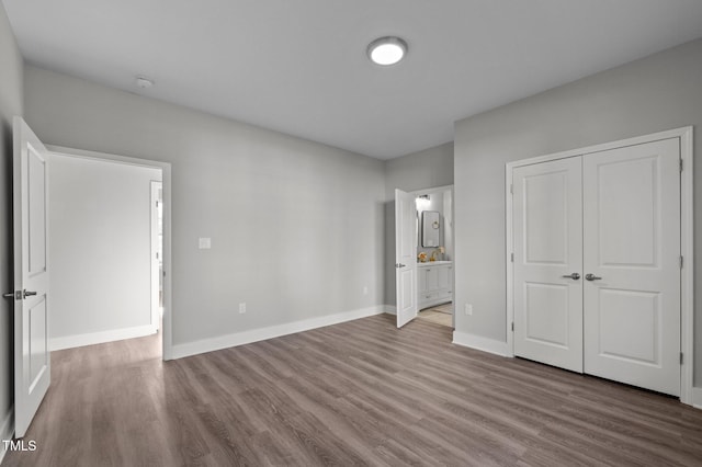 unfurnished bedroom featuring a closet, ensuite bath, wood finished floors, and baseboards