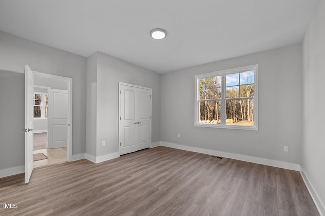 unfurnished bedroom with light wood-type flooring, baseboards, visible vents, and a closet