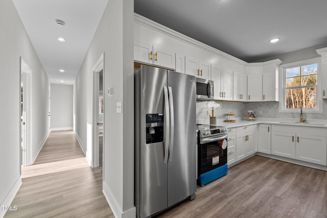 kitchen featuring stainless steel appliances, a sink, white cabinetry, light countertops, and light wood finished floors