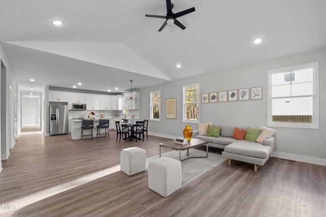 living area with light wood-style floors, vaulted ceiling, baseboards, and ceiling fan