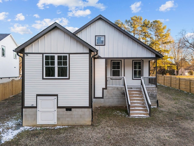 back of house featuring covered porch, stairway, fence, and board and batten siding