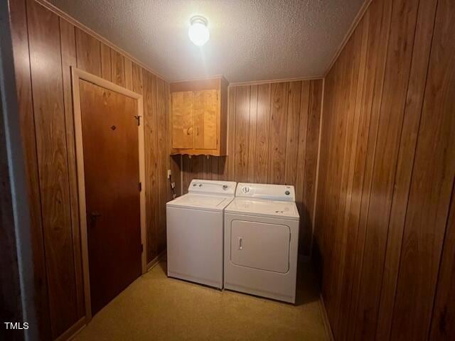 laundry room featuring a textured ceiling, wooden walls, washing machine and clothes dryer, and cabinets