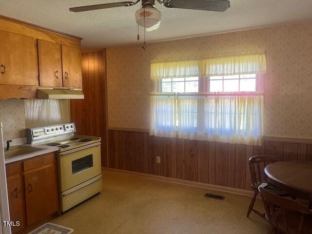 kitchen featuring a textured ceiling, wood walls, ceiling fan, and white electric range