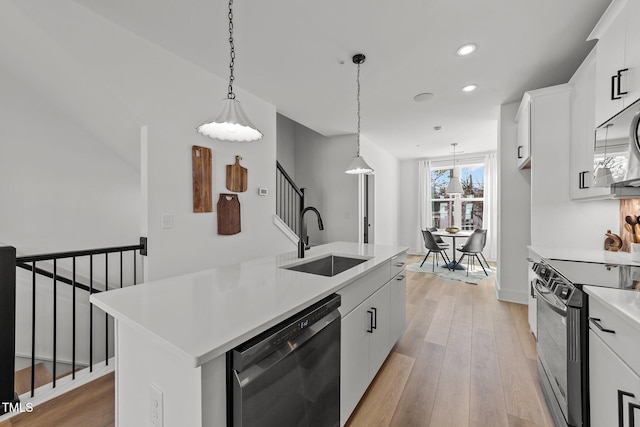 kitchen with sink, white cabinetry, black appliances, hanging light fixtures, and a kitchen island with sink