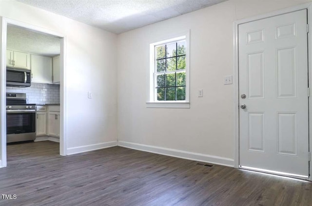 interior space with appliances with stainless steel finishes, backsplash, a textured ceiling, and dark wood-type flooring