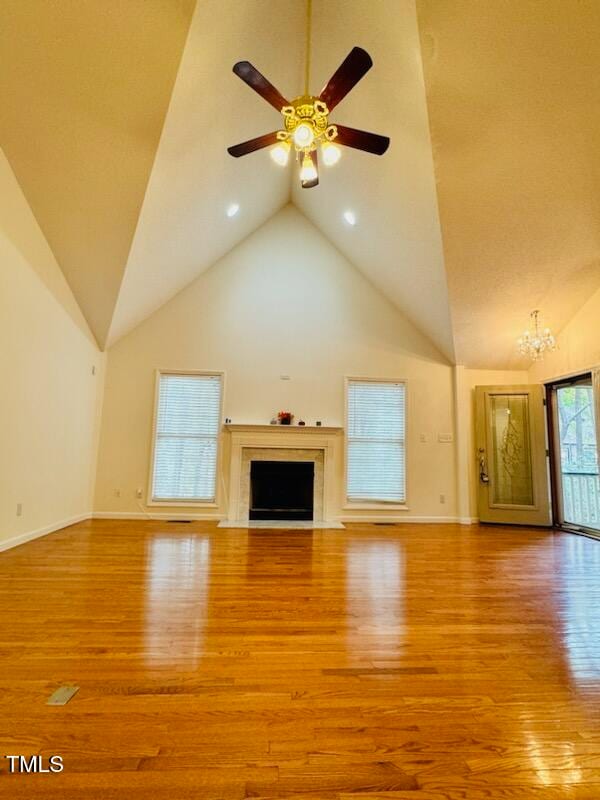 unfurnished living room with high vaulted ceiling, ceiling fan with notable chandelier, and light hardwood / wood-style flooring