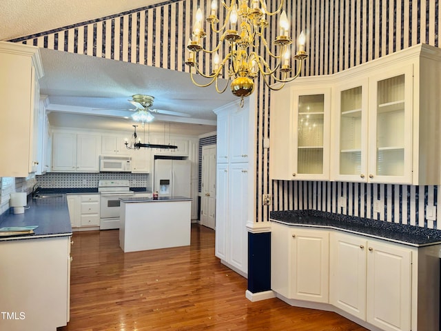 kitchen featuring a textured ceiling, decorative light fixtures, white cabinets, white appliances, and a center island