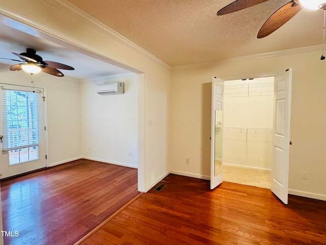 spare room featuring crown molding, a textured ceiling, a wall mounted air conditioner, dark wood-type flooring, and ceiling fan