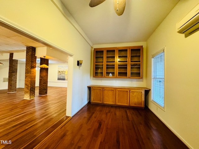 bar featuring ceiling fan, an AC wall unit, decorative columns, dark wood-type flooring, and pendant lighting