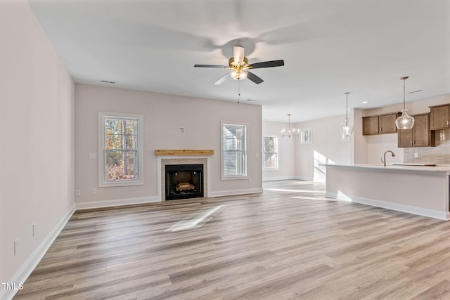 unfurnished living room with plenty of natural light, ceiling fan with notable chandelier, and light wood-type flooring