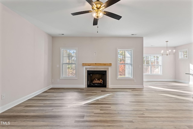 unfurnished living room with ceiling fan with notable chandelier, light hardwood / wood-style floors, and a tiled fireplace