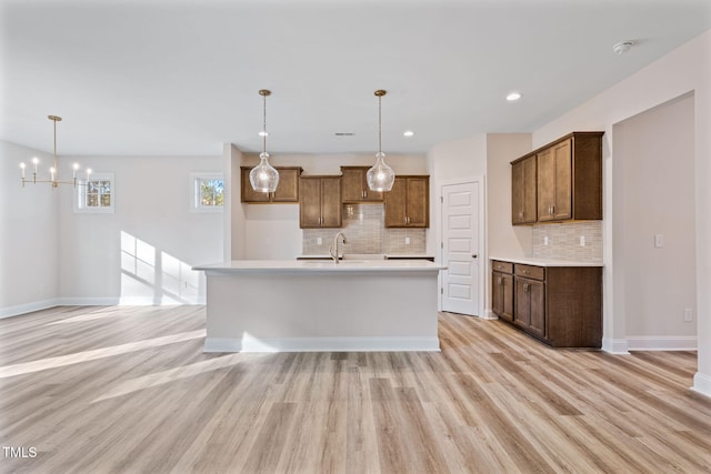 kitchen with light wood-type flooring, tasteful backsplash, a notable chandelier, hanging light fixtures, and an island with sink