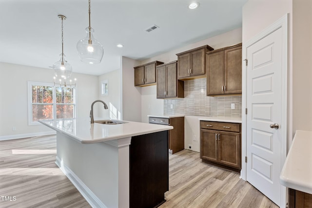 kitchen featuring backsplash, a kitchen island with sink, sink, decorative light fixtures, and light hardwood / wood-style floors