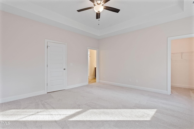 unfurnished bedroom featuring ceiling fan, a raised ceiling, light colored carpet, a walk in closet, and a closet