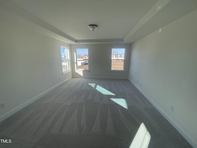 empty room with dark carpet, a raised ceiling, and ornamental molding