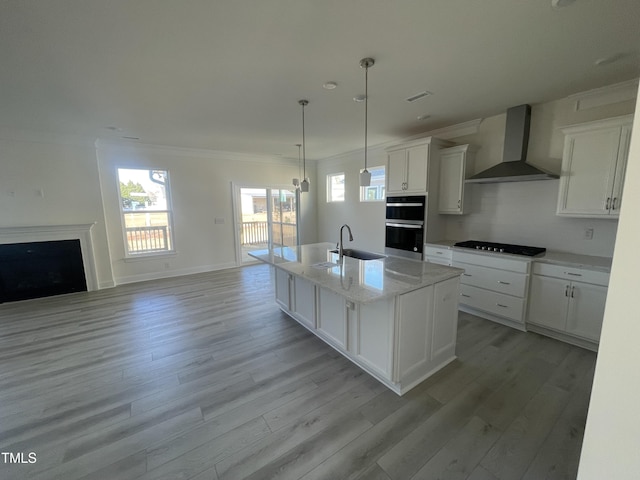 kitchen with white cabinetry, hanging light fixtures, wall chimney range hood, gas stovetop, and a kitchen island with sink