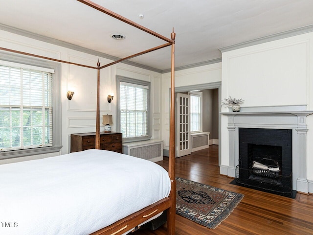 bedroom featuring dark hardwood / wood-style floors, radiator heating unit, crown molding, and a brick fireplace