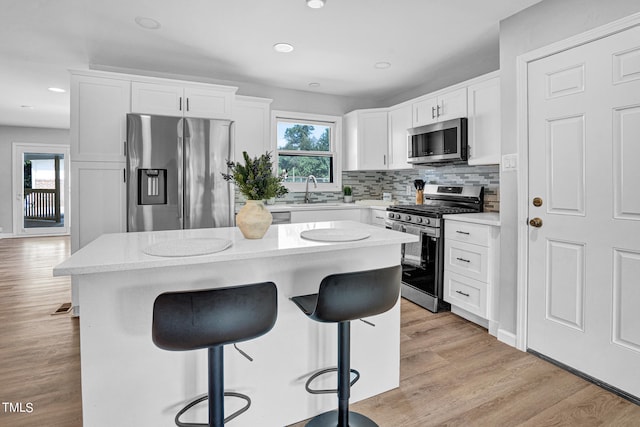 kitchen featuring tasteful backsplash, a kitchen island, white cabinetry, appliances with stainless steel finishes, and light hardwood / wood-style flooring