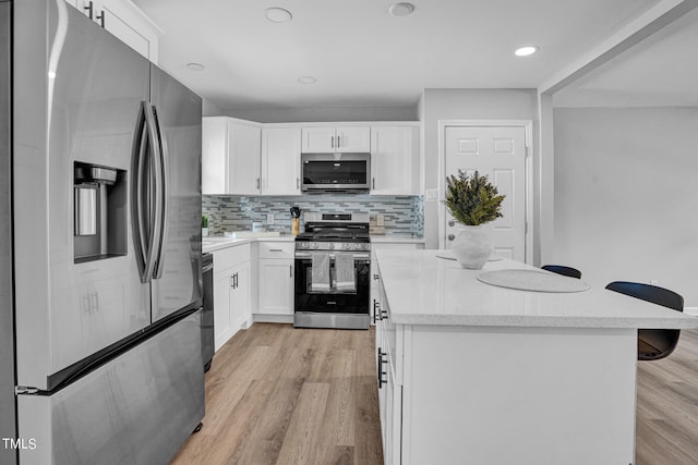 kitchen with backsplash, appliances with stainless steel finishes, white cabinets, light hardwood / wood-style floors, and a breakfast bar area