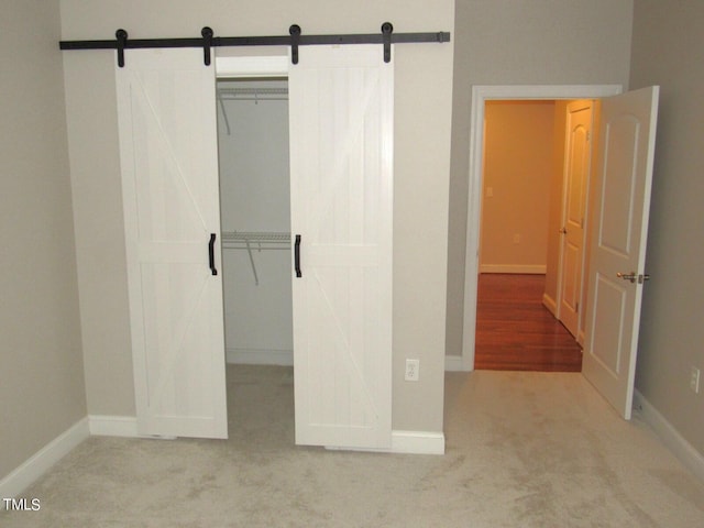 unfurnished bedroom featuring a barn door, light carpet, and a closet