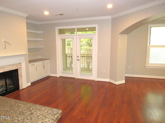 unfurnished living room featuring crown molding, a stone fireplace, dark hardwood / wood-style flooring, and french doors