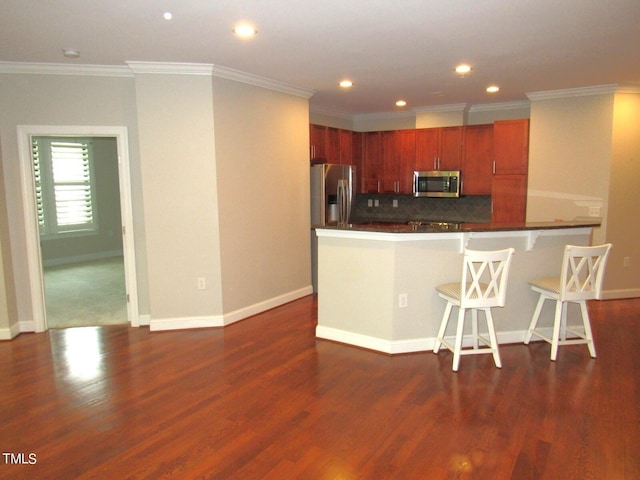 kitchen featuring a breakfast bar area, crown molding, appliances with stainless steel finishes, dark hardwood / wood-style floors, and backsplash