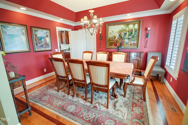 dining space with a notable chandelier, light wood-type flooring, ornamental molding, and a healthy amount of sunlight