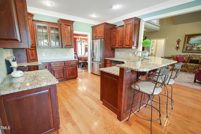 kitchen featuring appliances with stainless steel finishes, light hardwood / wood-style floors, light stone counters, backsplash, and kitchen peninsula