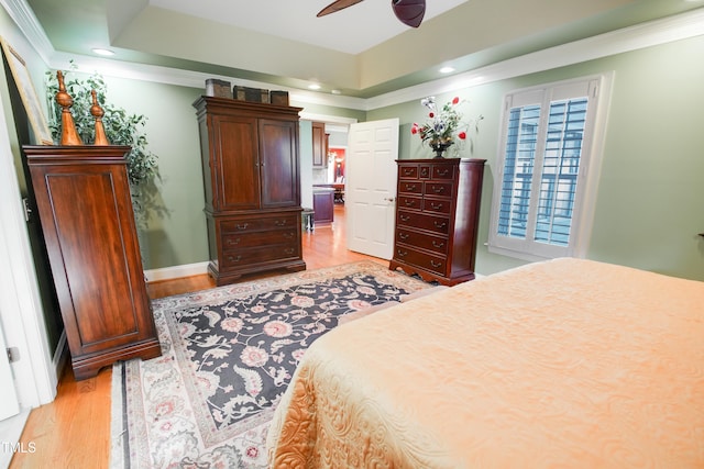 bedroom with ornamental molding, light wood-type flooring, ceiling fan, and a raised ceiling