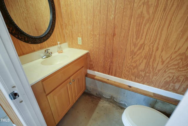 bathroom with wooden walls, concrete flooring, vanity, and toilet