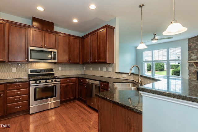 kitchen with sink, kitchen peninsula, appliances with stainless steel finishes, dark hardwood / wood-style floors, and decorative light fixtures