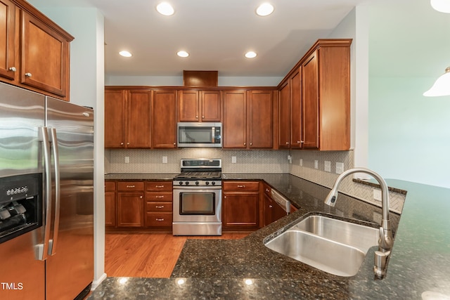 kitchen with appliances with stainless steel finishes, dark stone counters, sink, and light hardwood / wood-style flooring