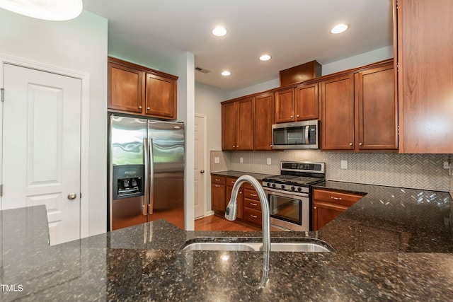 kitchen with dark stone countertops, decorative backsplash, sink, and stainless steel appliances