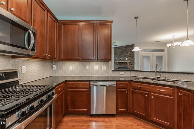 kitchen featuring stainless steel appliances, sink, decorative light fixtures, and light hardwood / wood-style flooring