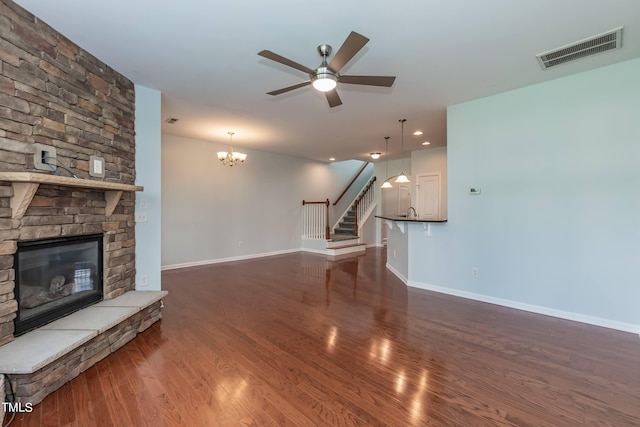 unfurnished living room featuring a stone fireplace, dark wood-type flooring, and ceiling fan with notable chandelier